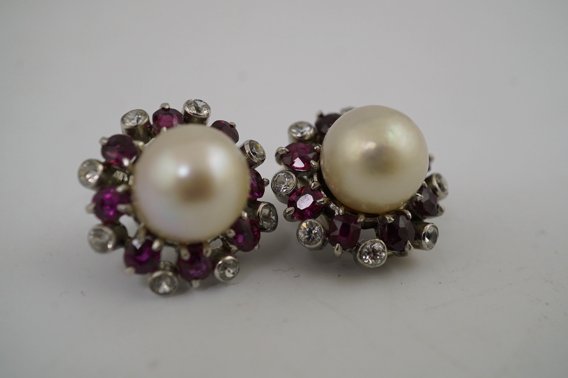 A pair of pearl earrings, with ruby and simuluated diamond surrounds, unmarked, 8.2 g gross. Condition - fair